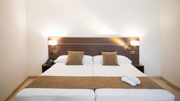 Habitación de hotel con una cama grande, dos mesitas de noche y un cabecero con lámparas de pared.