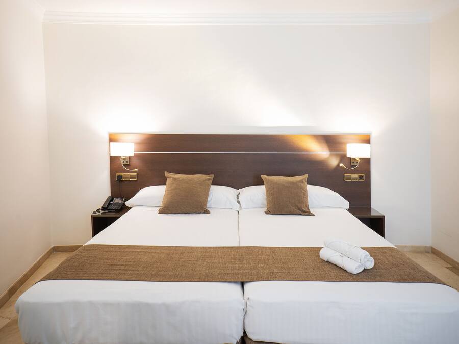 Habitación de hotel con una cama grande, dos mesitas de noche y un cabecero con lámparas de pared.