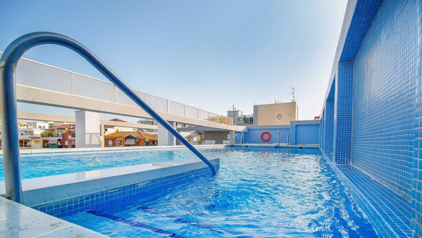 A swimming pool with a blue tiled interior, a metal handrail, and a view of buildings in the background. - Hotel Mainake (Velez-Malaga)