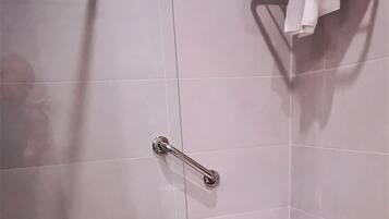 A shower area with a glass door, a handrail, a towel rack, and a small bench.