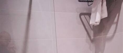 Zona de ducha con puerta de cristal, barra de apoyo, toallero y un pequeño banco.