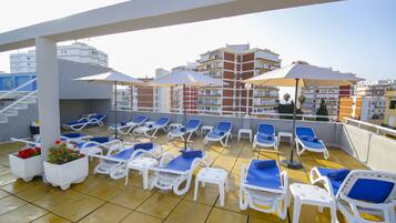 Eine Dachterrasse mit Liegestühlen, Sonnenschirmen und Topfpflanzen.