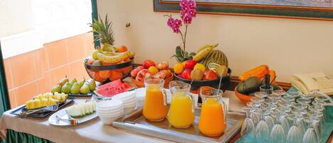 A buffet table with various fruits, a pitcher of orange juice, and several glasses.