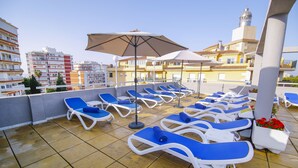 A rooftop terrace with blue lounge chairs and umbrellas, overlooking a cityscape with buildings and a tower. - Hotel Mainake (Velez-Malaga)