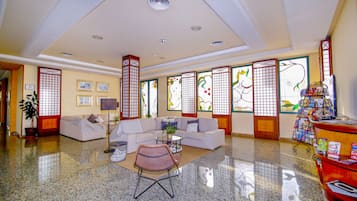 Un vestíbulo amplio con piso de granito pulido, un sofá blanco, un sillón de mimbre y un mostrador de recepción rojo.
