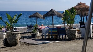 A beachside seating area with umbrellas, lounge chairs, and potted plants. - Hotel Mainake (Velez-Malaga)