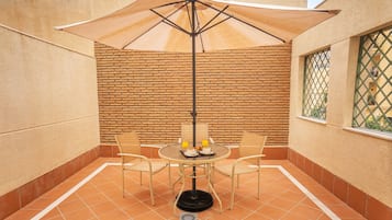 Eine Terrasse mit einem runden Tisch, vier Stühlen, einem Sonnenschirm und einer Ziegelwand.