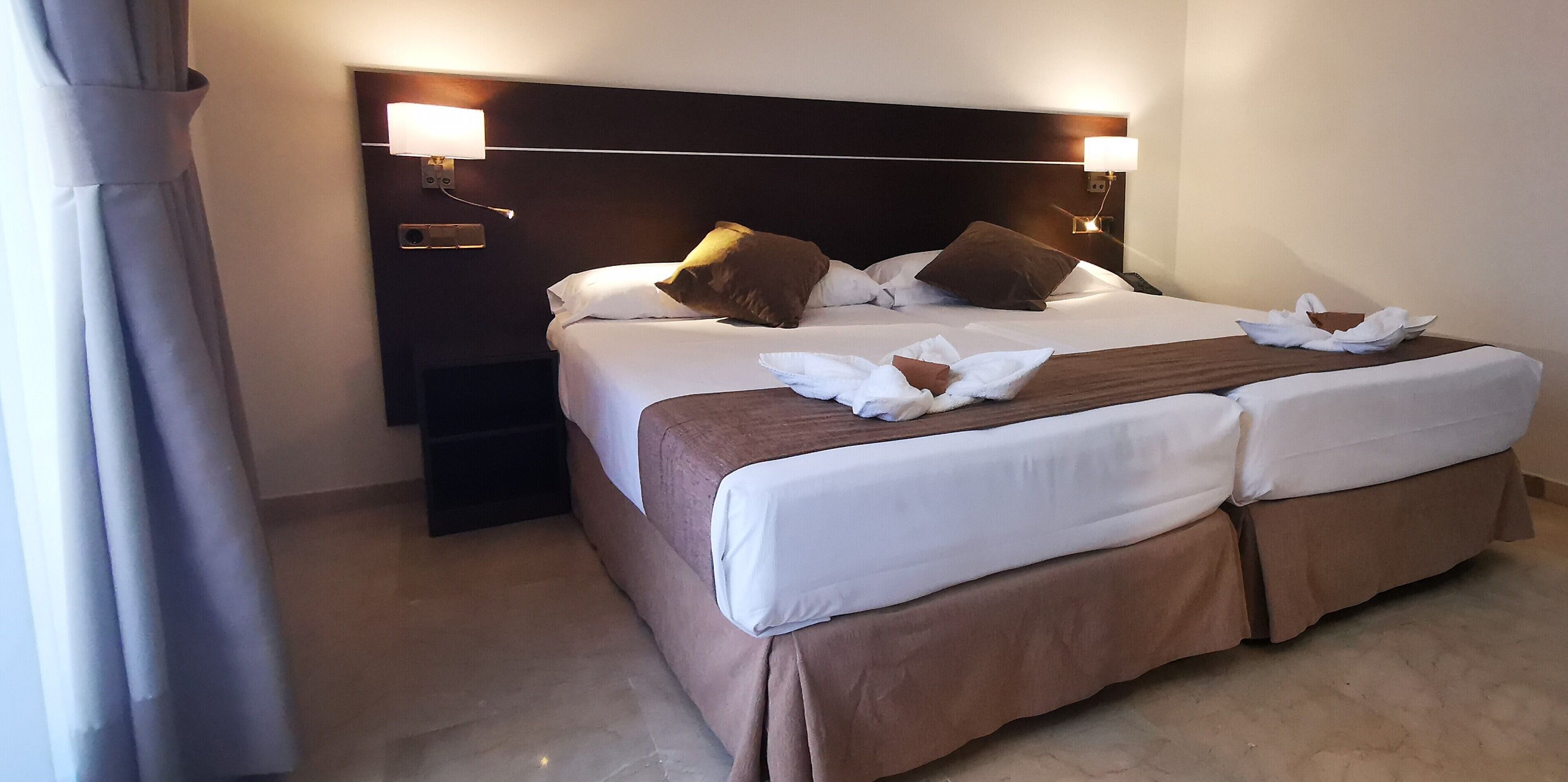 A hotel room with a large bed, two bedside lamps, and a nightstand.