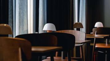 Una hilera de mesas y sillas de madera en una habitación con poca luz, ventanas grandes y cortinas.