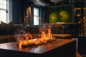 Un interior moderno con una mesa de vidrio que exhibe rocas y llamas, un sofá de cuero y una pared verde con una planta.