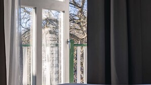Et værelse med en seng, et vindue med gardiner og udsigt til træer og en bygning.