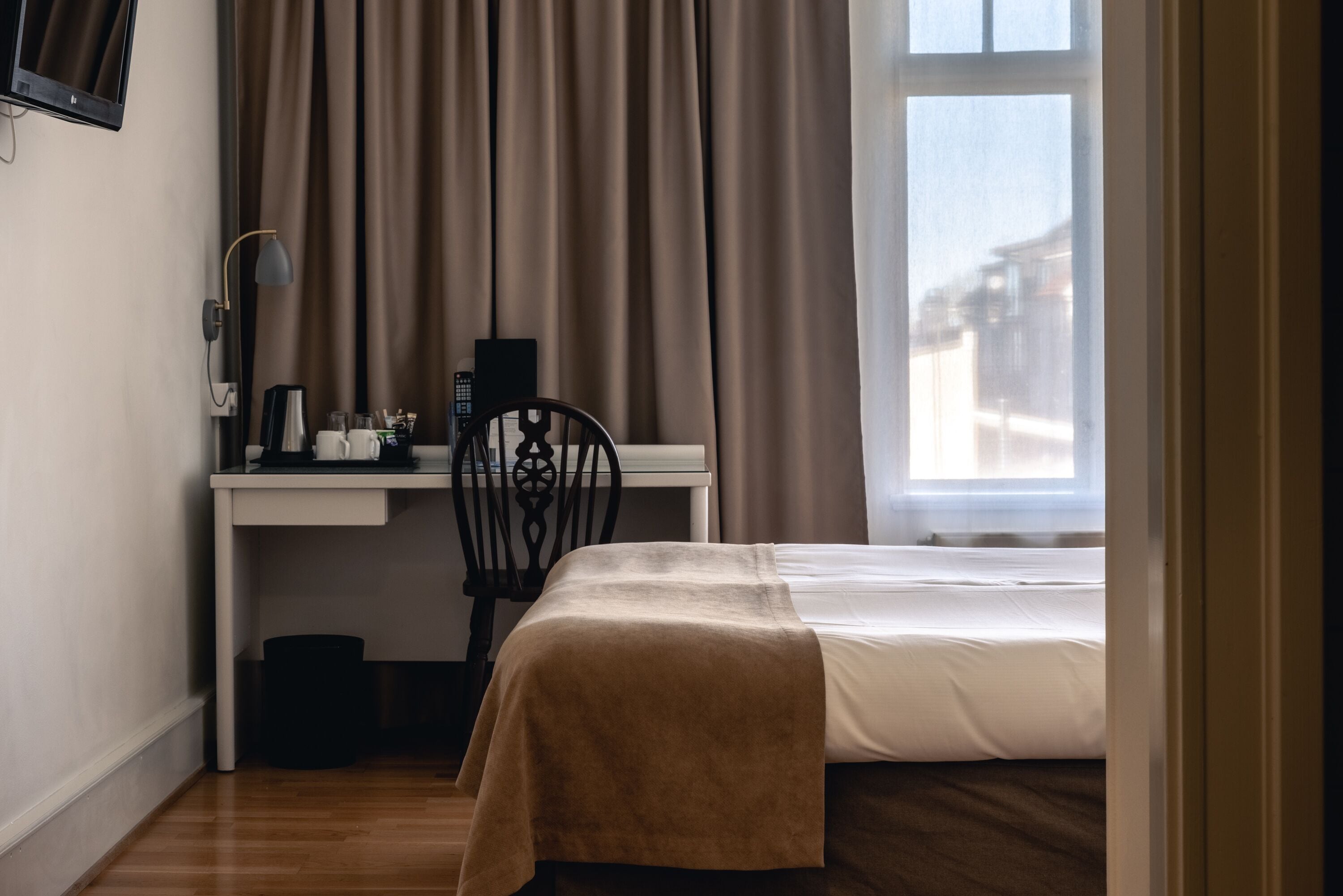 A hotel room with a bed, a desk with a chair, a coffee maker, and a window with curtains.