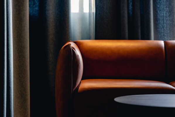 Un sofá de cuero con una mesa redonda en una habitación poco iluminada con cortinas.