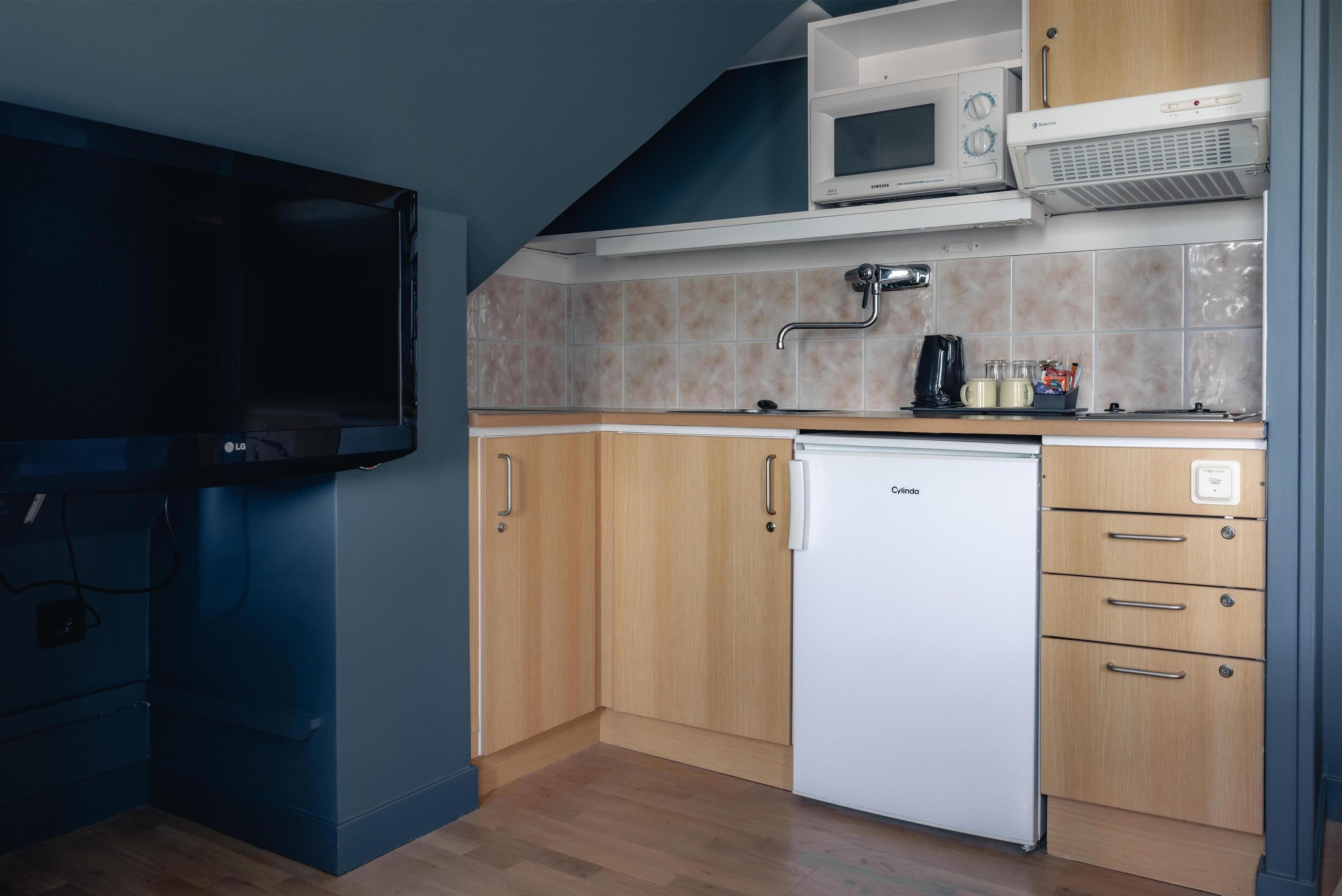 Cocina compacta con microondas, refrigerador y un lavamanos pequeño.