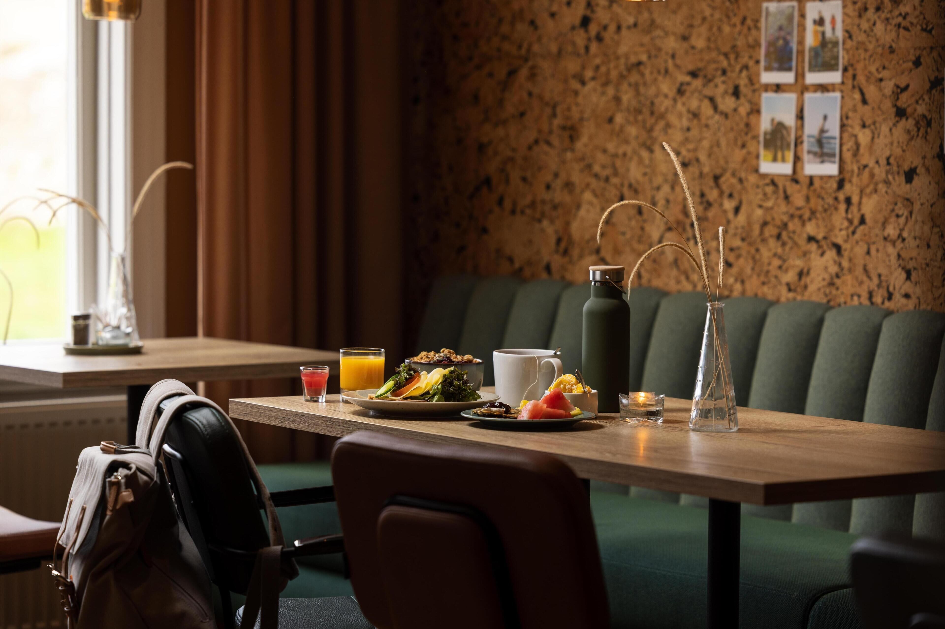 Un comedor con una mesa de madera dispuesta para el desayuno, incluyendo un plato de comida, un vaso de jugo de naranja y una jarra.