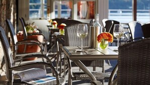A restaurant with outdoor seating, wicker chairs, tables with wine glasses, and a view of the water. - Trident Hotel (Kinsale)