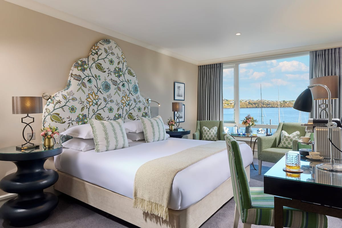 A hotel room with a large bed, a view of the sea, a dining area, and a sitting area with a view.