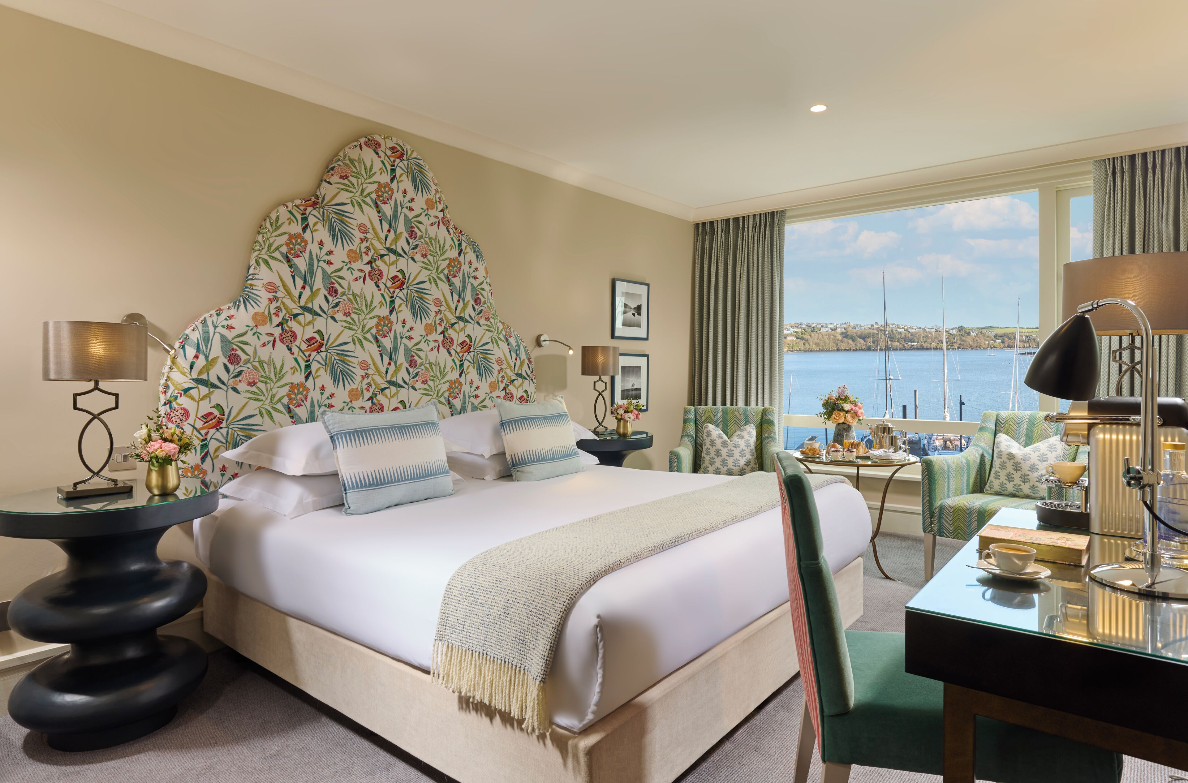 A hotel room with a bed, a desk, a chair, a view of the sea, and a window with curtains.