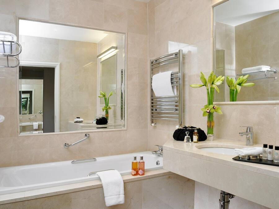 A modern bathroom with a bathtub, a sink, and two mirrors. There are toiletries on the sink counter, and a towel rack with a towel hanging on it.