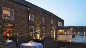 An outdoor dining area with round tables and chairs, set against a stone building with multiple windows. - Trident Hotel (Kinsale)