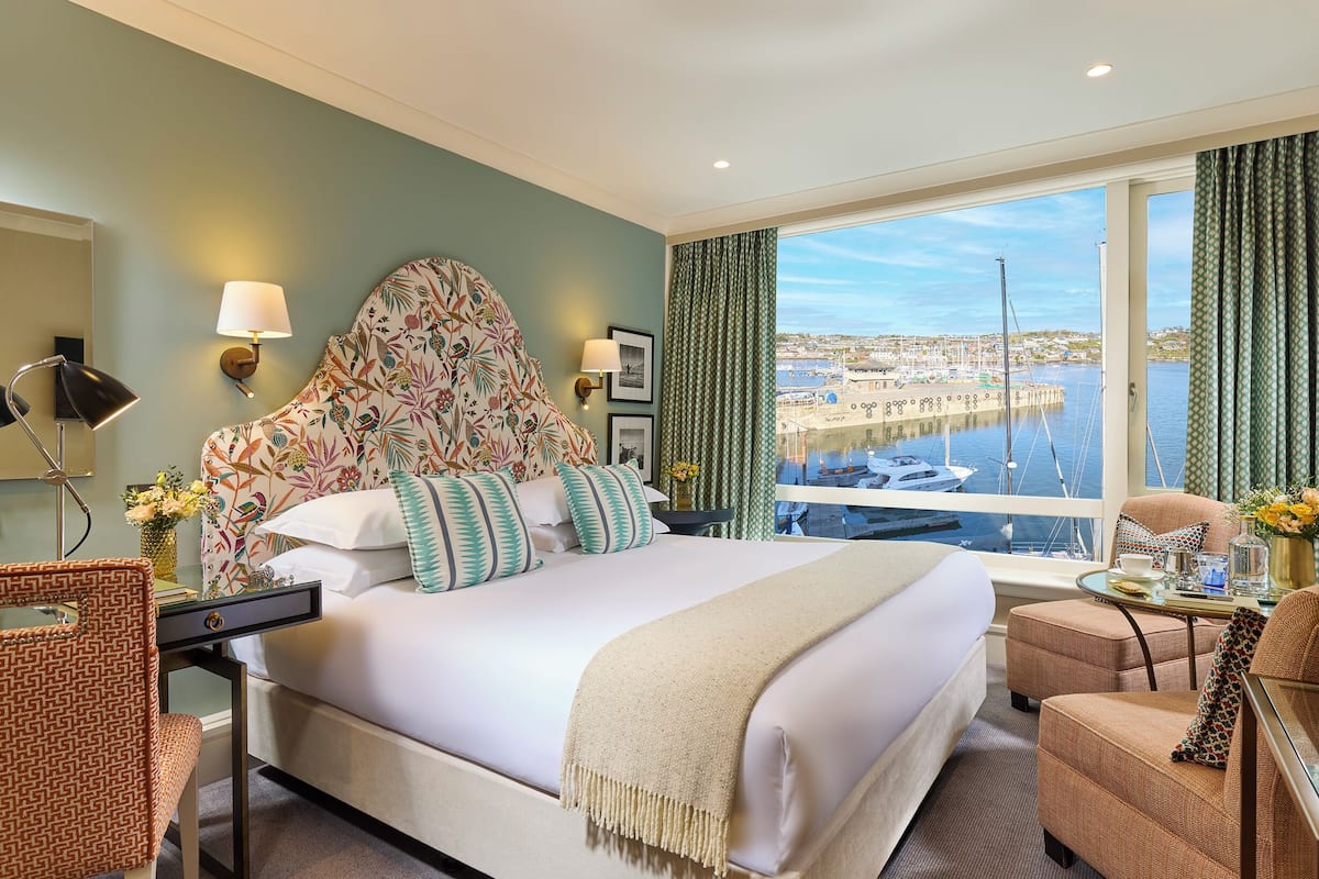 A hotel room with a large bed, a desk, and a view of a marina.