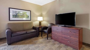 Ein Hotelzimmer mit einer Couch, einem Fernseher auf einer Holzkabine, einer Lampe und einem gerahmten Bild an der Wand.