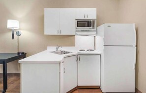A compact kitchen with white cabinets, a microwave, a stove, and a refrigerator.