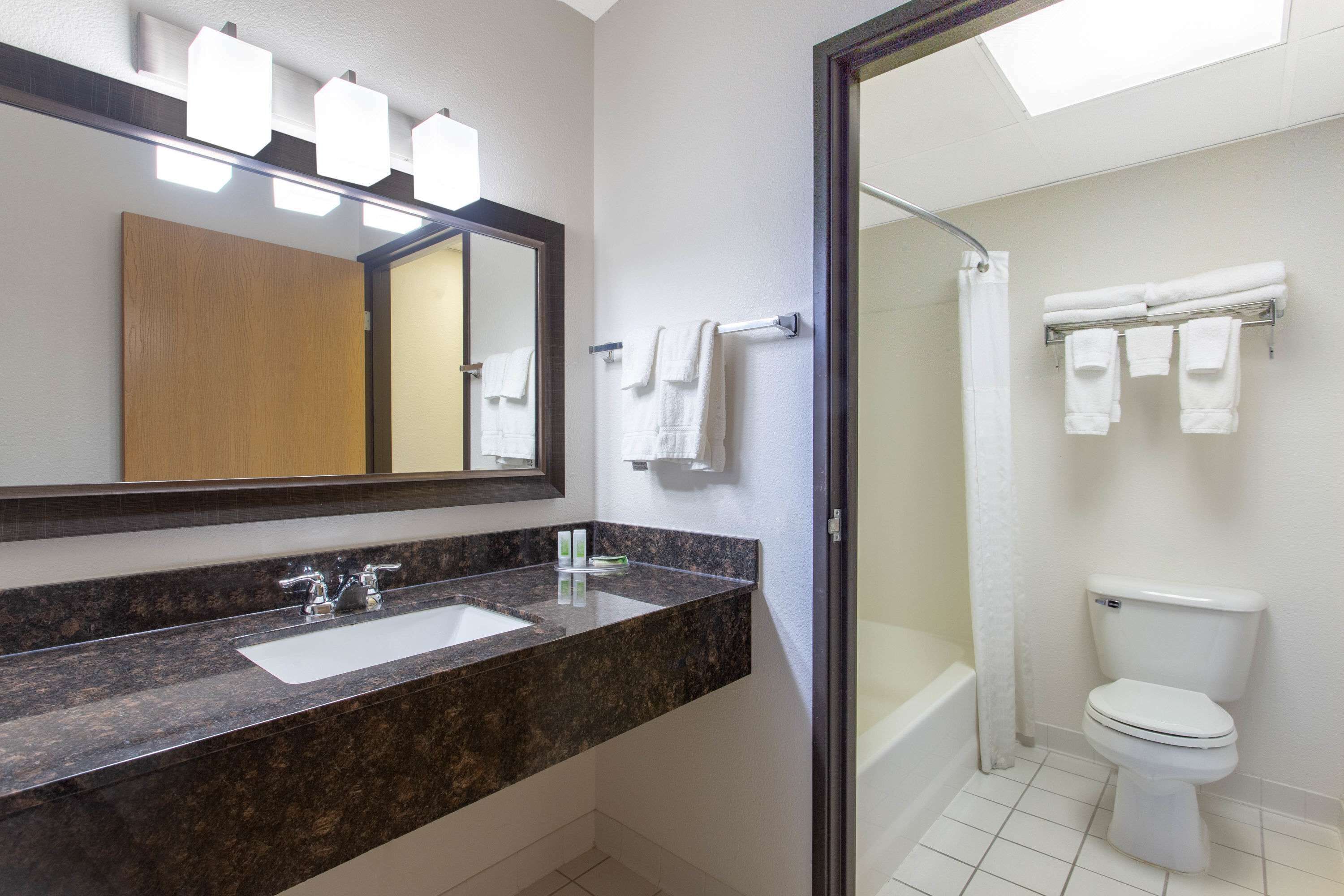 Un baño moderno con lavamanos de granito, un espejo grande y ducha con mampara de vidrio.