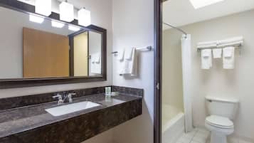 Un baño moderno con lavamanos de granito, un espejo grande y ducha con mampara de vidrio.