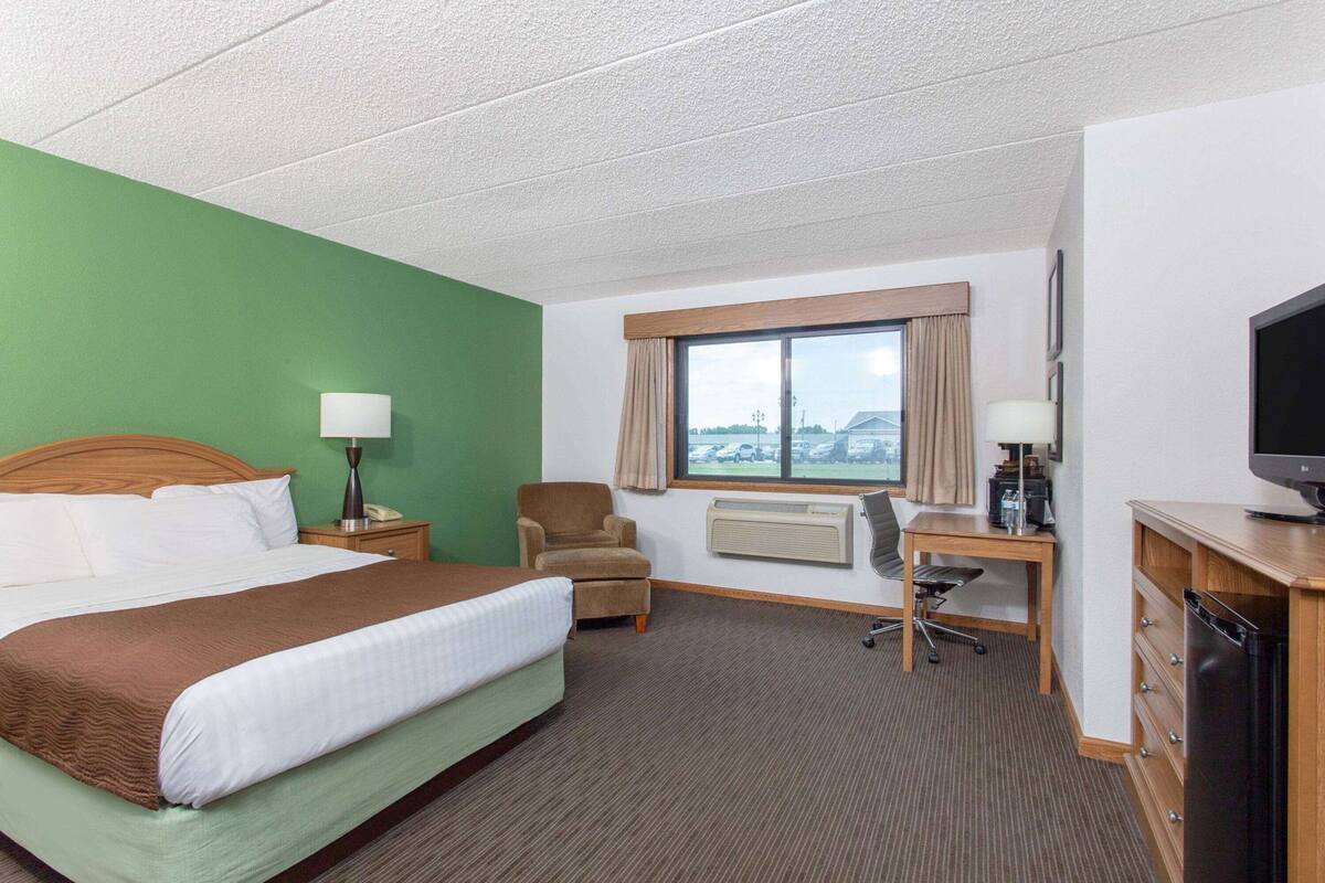 Habitación de hotel con cama, escritorio, silla, televisión y ventana con vistas.