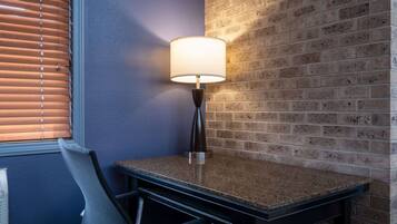 Una esquina de habitación con una mesa, una silla, una lámpara y un muro de ladrillo.