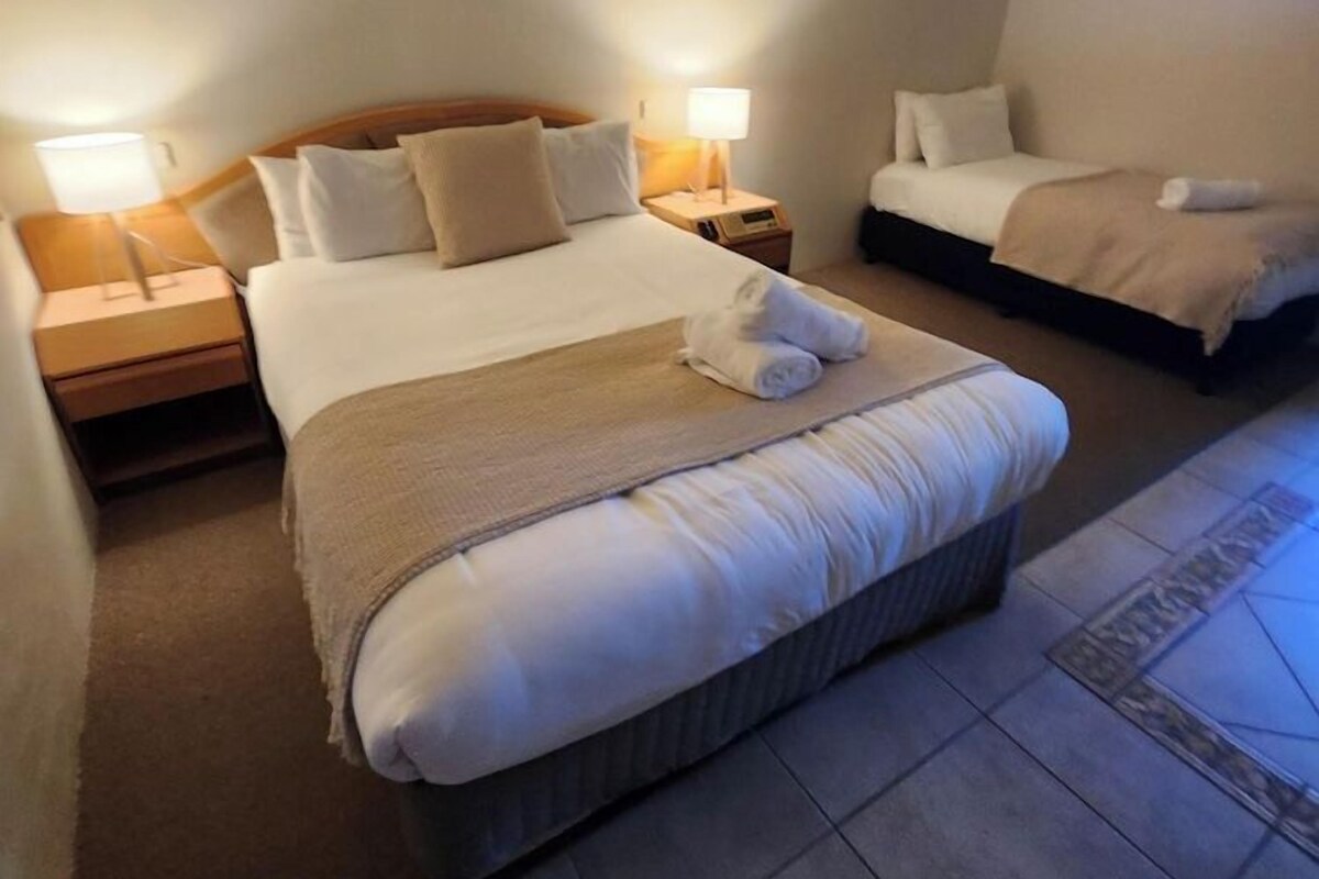 Une chambre d’hôtel avec un grand lit, un lit plus petit, deux tables de chevet avec des lampes et un tableau au mur.