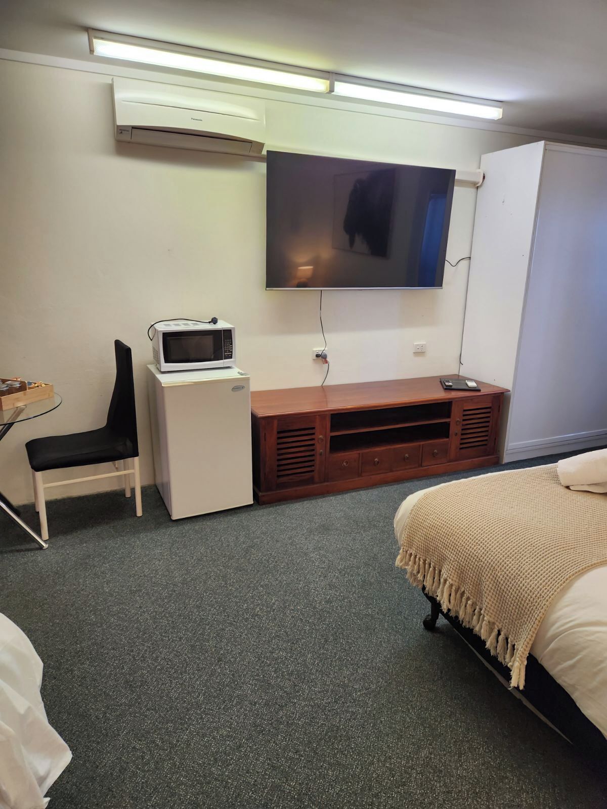 A hotel room with a bed, a desk with a computer, a microwave, and a TV mounted on the wall.