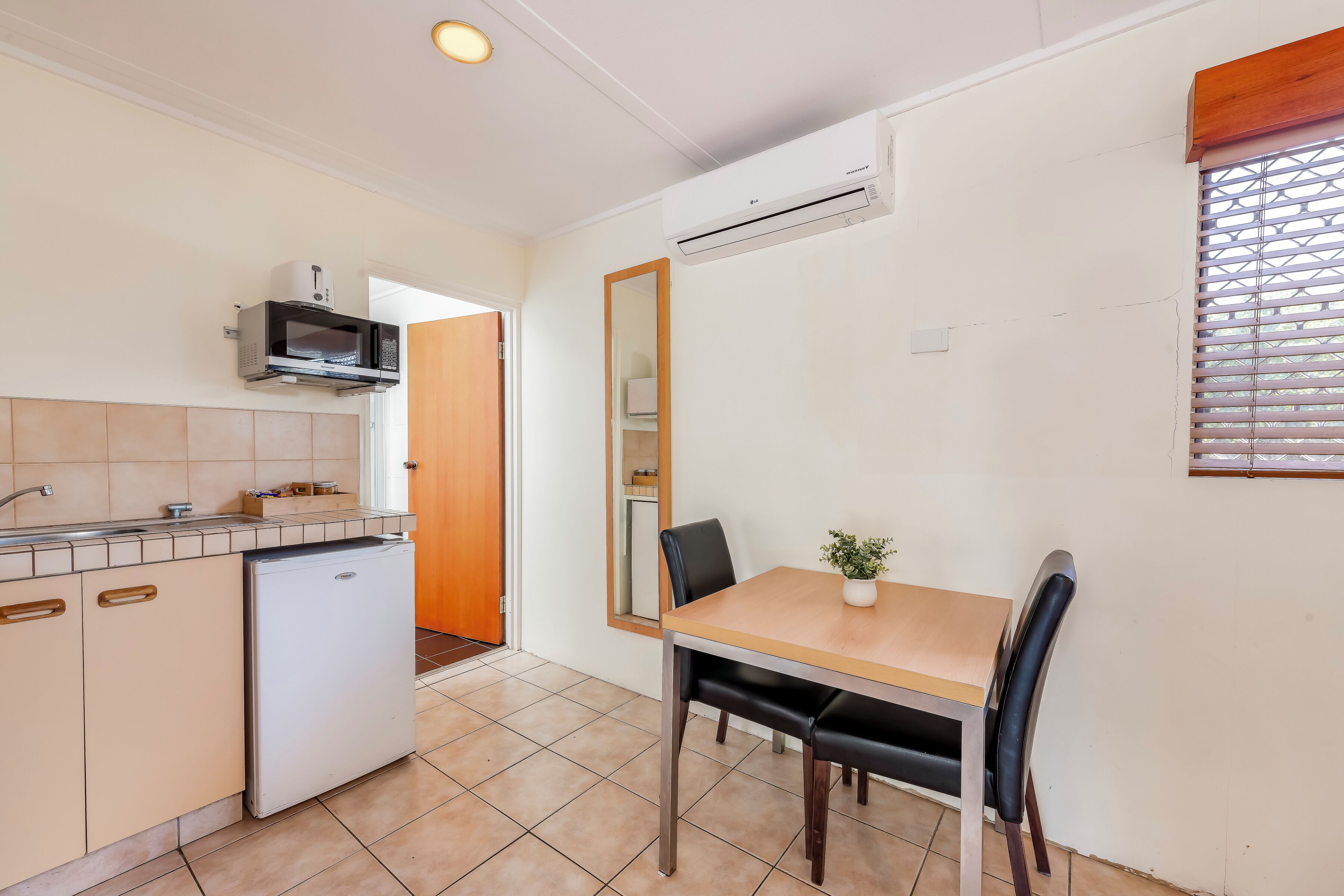Cocina compacta con microondas, refrigerador y comedor con mesa y sillas.