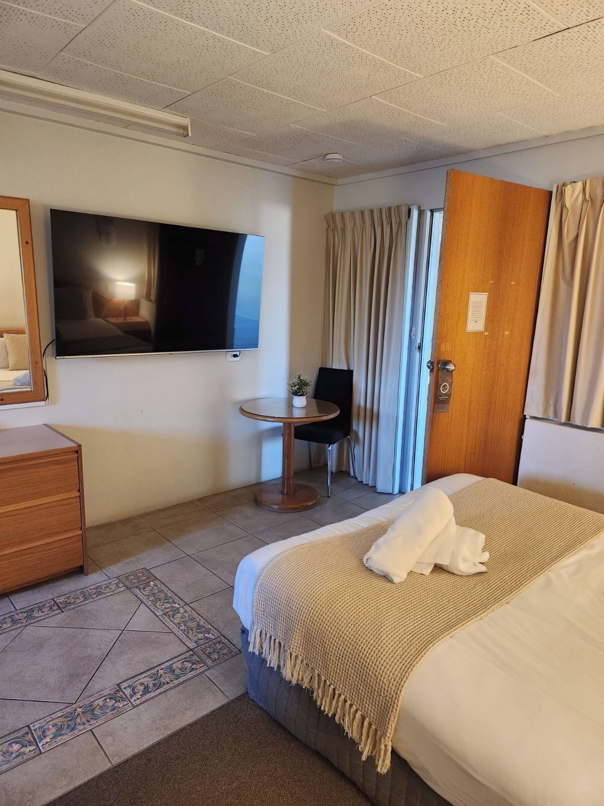 Una habitación de hotel con cama, escritorio, silla, televisor y puerta.