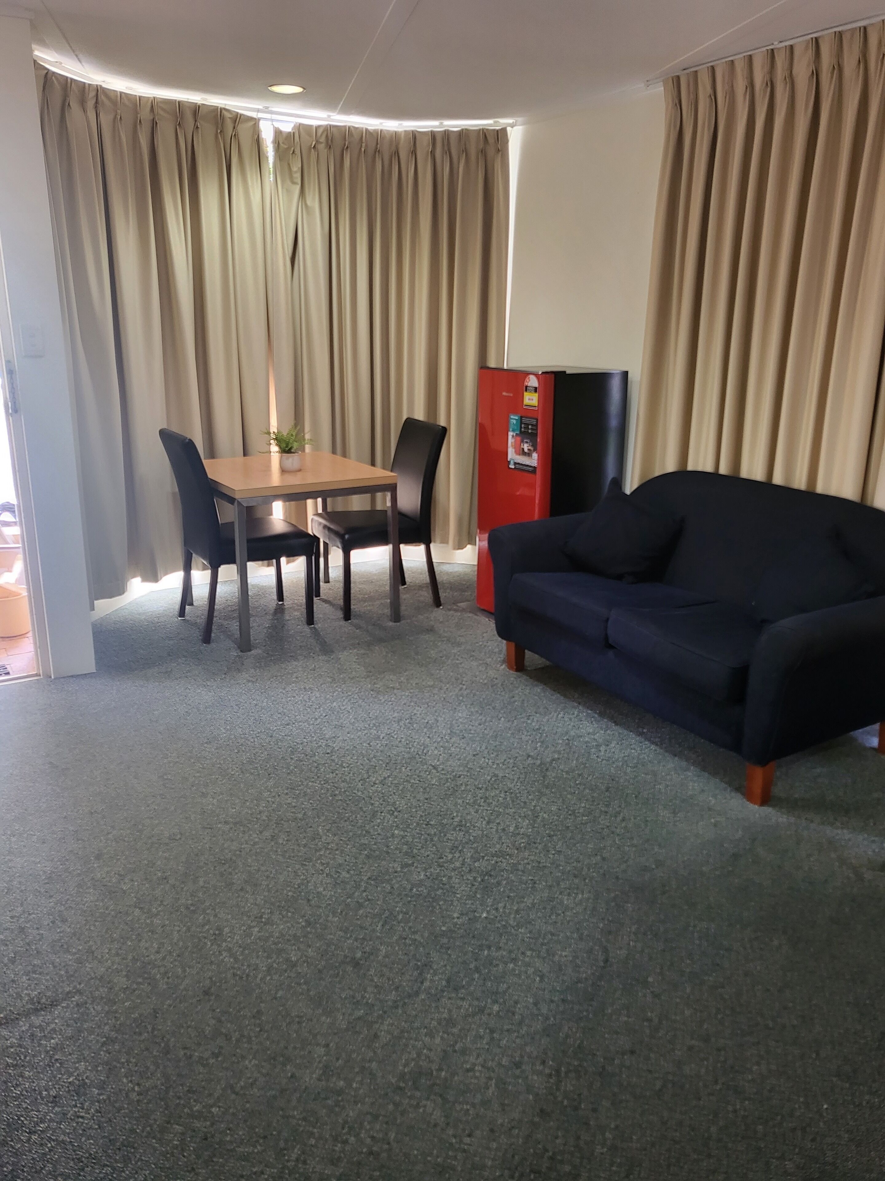 A room with a dining table, chairs, a sofa, a refrigerator, and curtains.