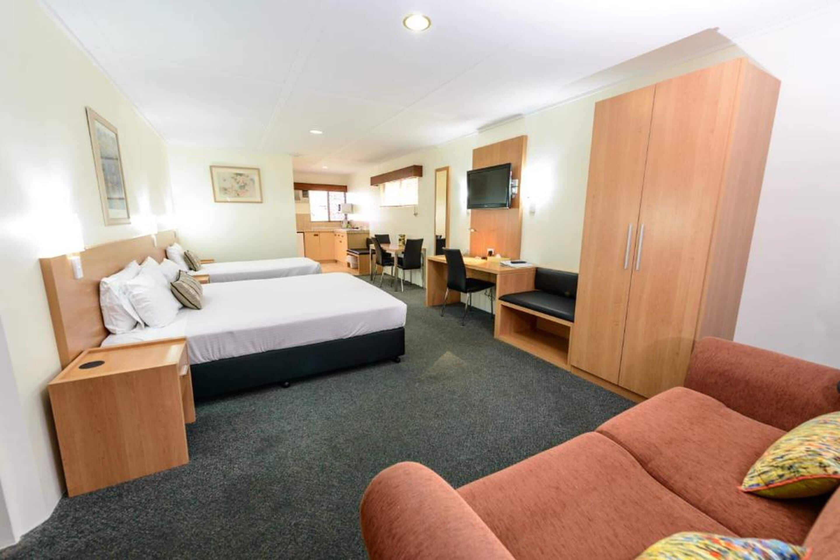 A hotel room with two beds, a desk, a TV, and a wardrobe.