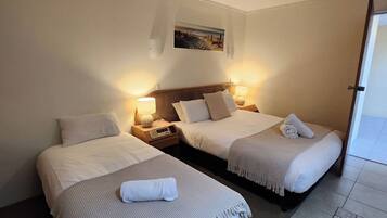 A hotel room with two beds, each with a bedside table and lamp, a small painting on the wall, and a tiled floor with a decorative border.