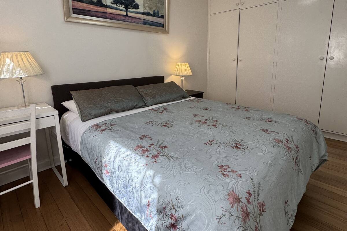 Un dormitorio con una cama, dos lámparas de noche, un cuadro en la pared y un armario.