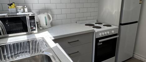 A modern kitchen with a stainless steel sink, a microwave, a kettle, a stove, and a refrigerator.
