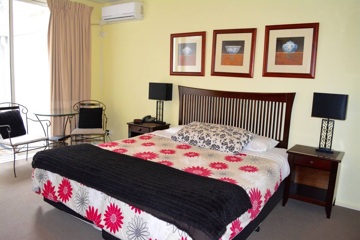 Habitación de hotel ordenada con una cama, dos mesitas de noche, una silla y un escritorio.