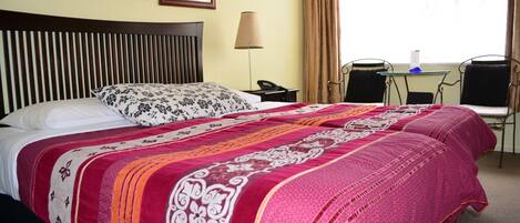 A hotel room with a large bed, two bedside tables, a lamp, a chair, and a window with curtains.