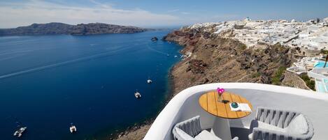 A balcony with a table and two chairs overlooking a coastal town with clear blue waters and boats.