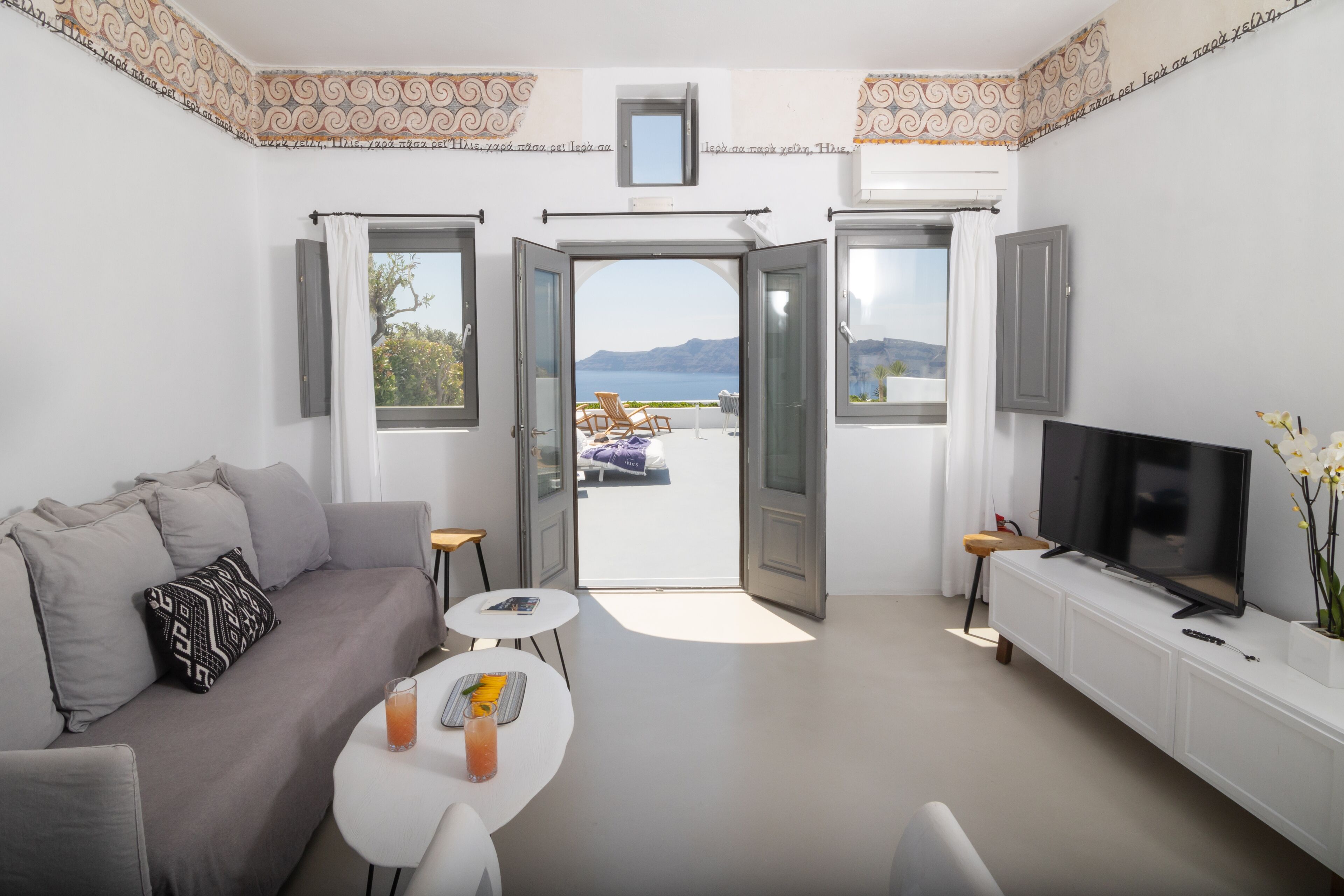 Una sala de estar moderna con un sofá, una mesita con una bebida, un televisor y vistas al exterior.