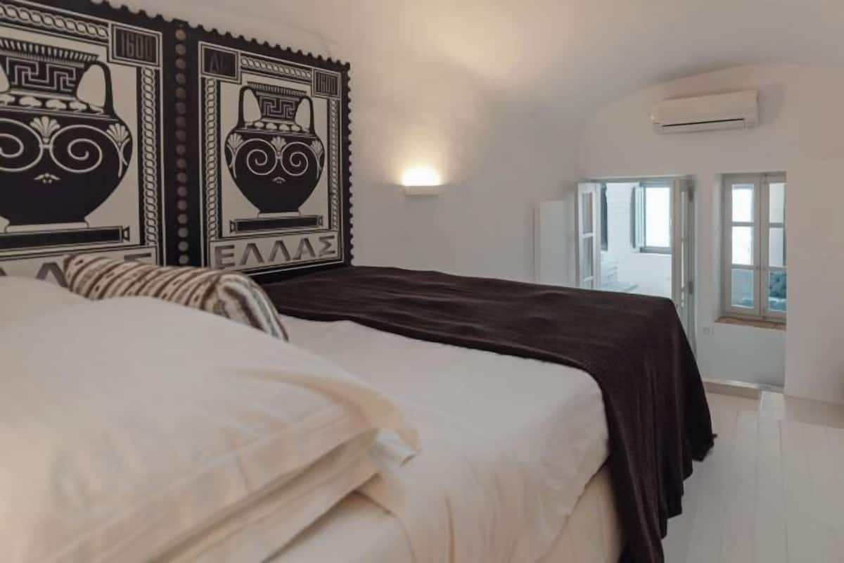 A bedroom with a bed, two wall-mounted air conditioning units, and a window with a view.