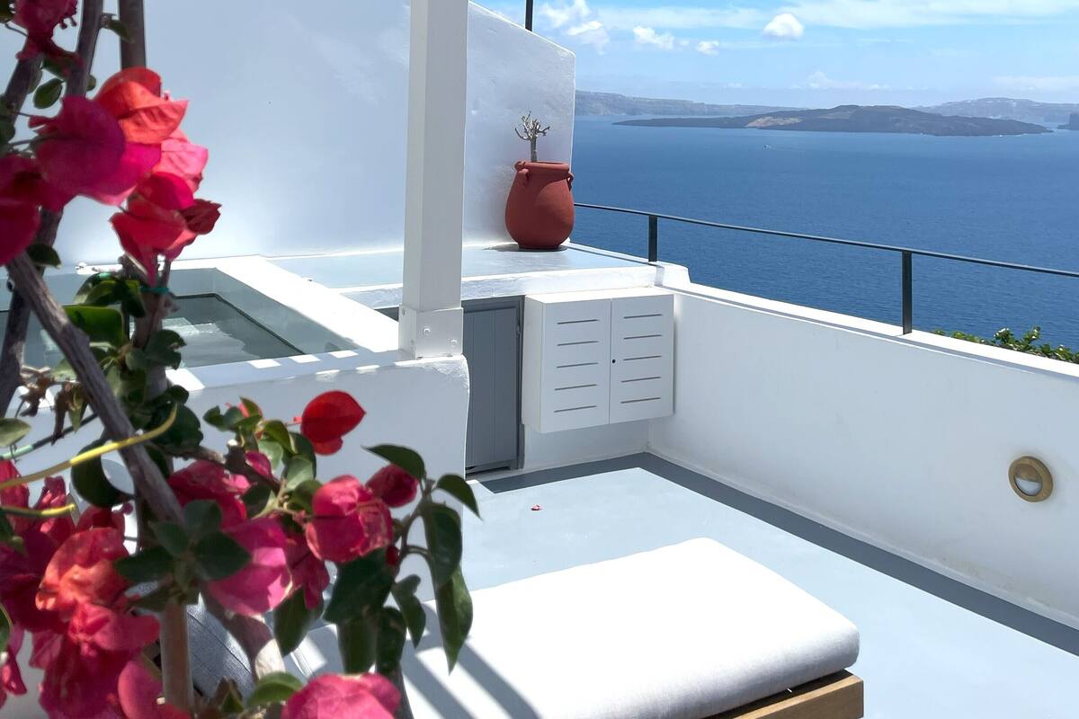 A balcony with a white pergola, a potted plant, and a view of the sea.