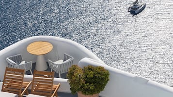 A pool area with lounge chairs and a table, surrounded by a white deck overlooking a body of water.