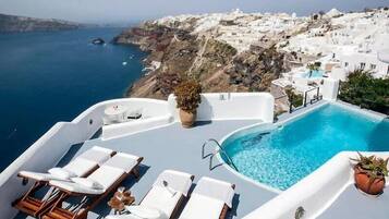 A rooftop pool with white lounge chairs and a view of a coastal town.