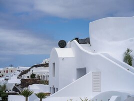 Un edificio de paredes blancas con una escalera que lleva a una puerta, rodeado de palmeras y otros edificios blancos.