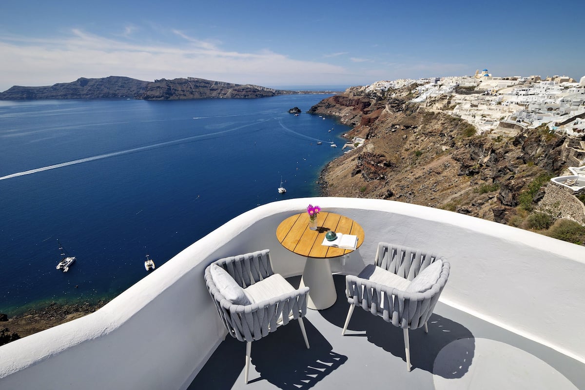 A terrace with a table and two chairs overlooking a coastal area with boats and a distant island.